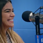 Karol G sonriendo en un estudio de radio, con auriculares y micrófono