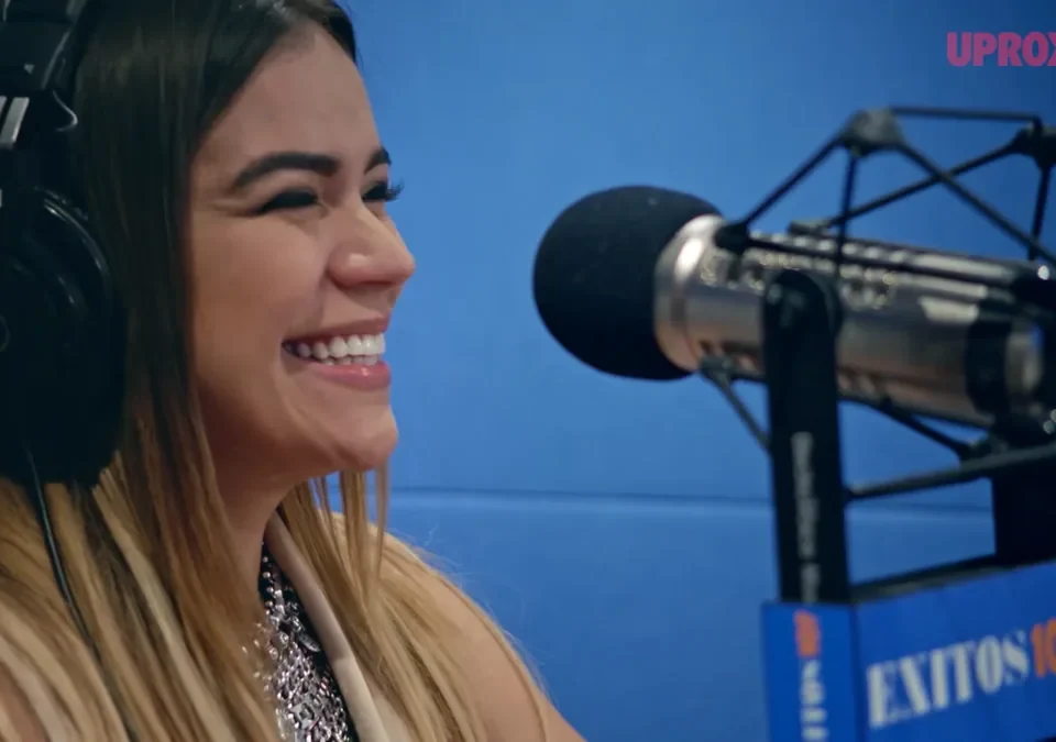 Karol G sonriendo en un estudio de radio, con auriculares y micrófono