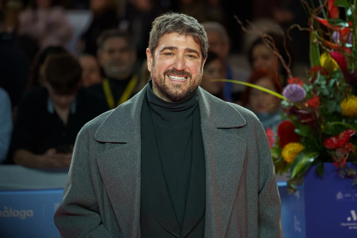 Antonio Orozco sonríe con abrigo gris y jersey de cuello alto ante una fila de fotógrafos