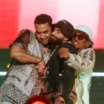 Arcángel, con gorra, abrazado a Don Omar y Tego Calderón sobre un escenario