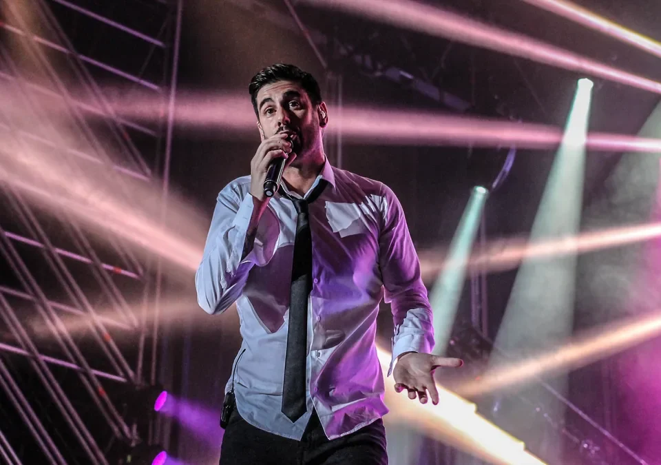 Melendi cantando en un concierto con focos de colores al fondo