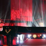 Pablo López cantando al piano sobre un escenario iluminado en rojo