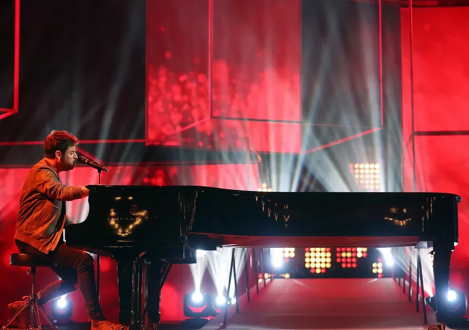 Pablo López cantando al piano sobre un escenario iluminado en rojo
