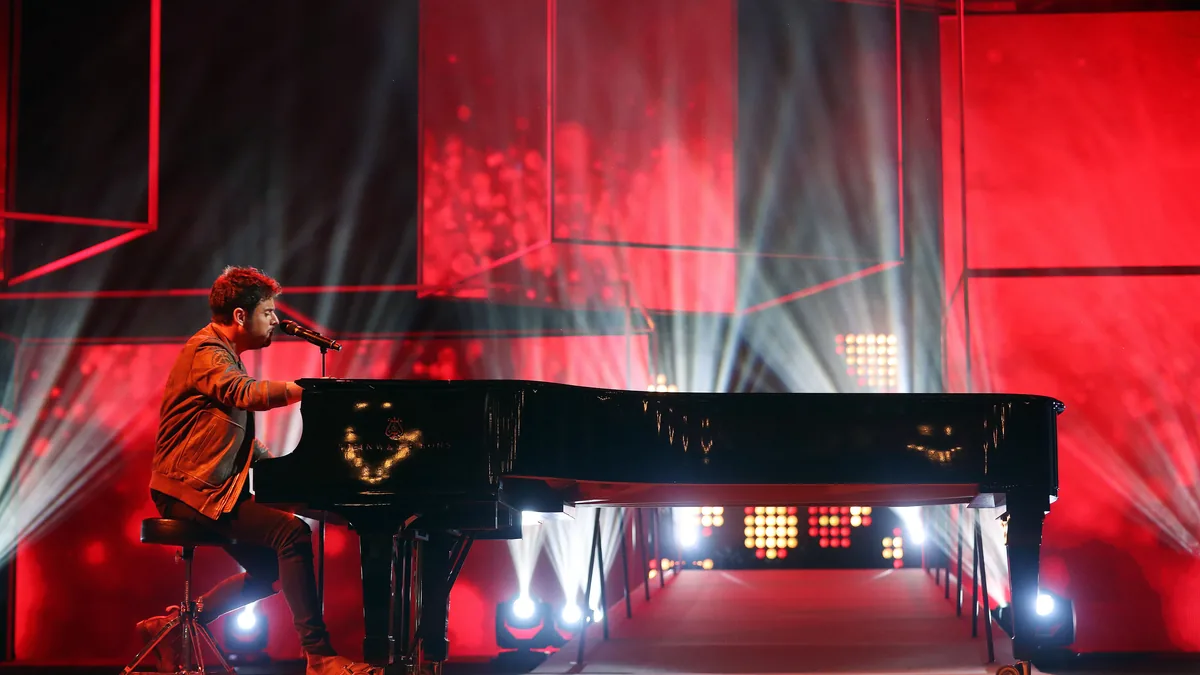 Pablo López canta sentado al piano de cola sobre un escenario iluminado en rojo
