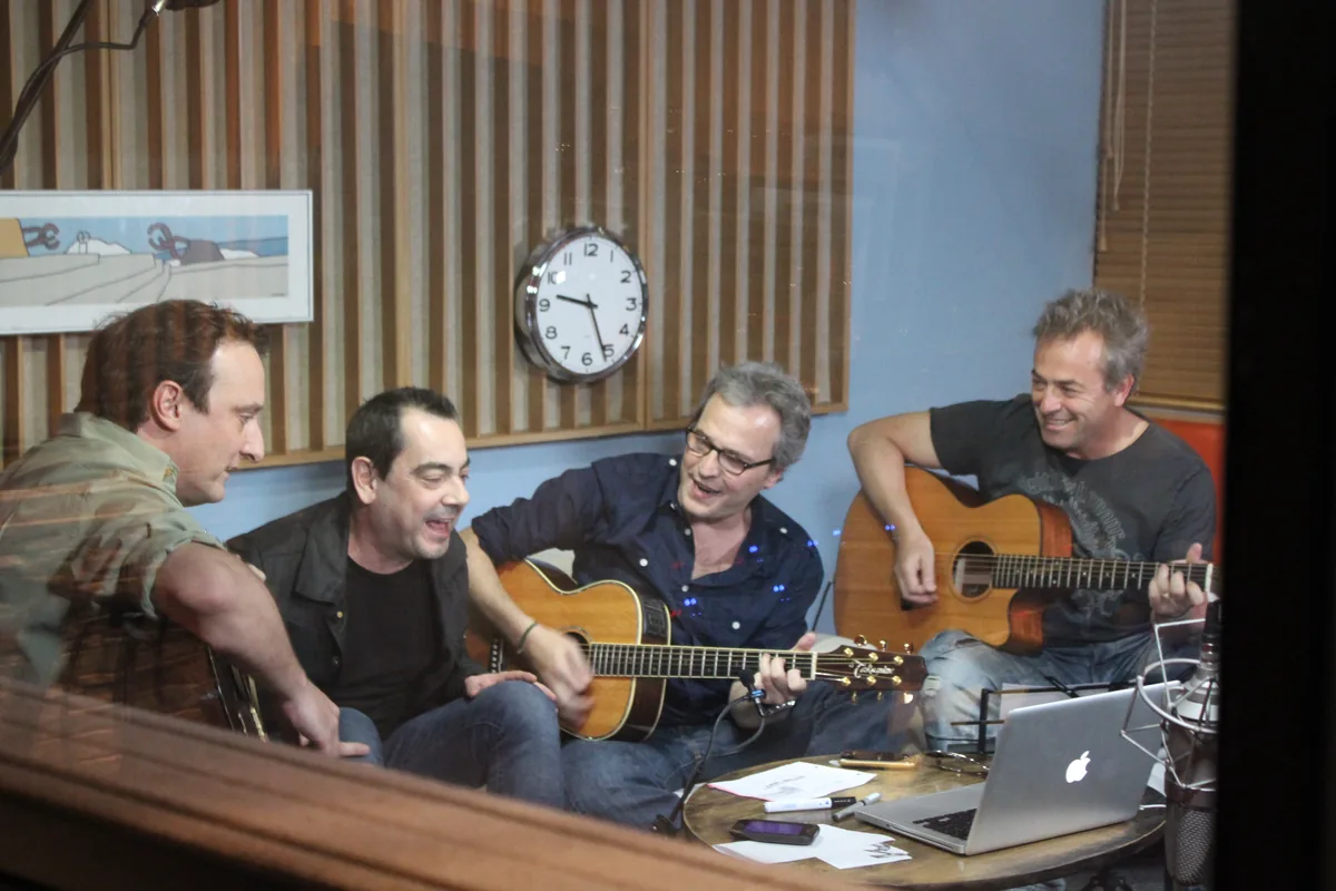 Los cuatro miembros de Hombres G tocando con guitarras acústicas en un estudio
