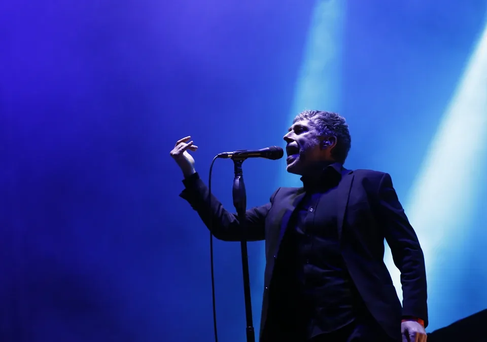 Iván Ferreiro cantando ante el micrófono bajo una luz azul