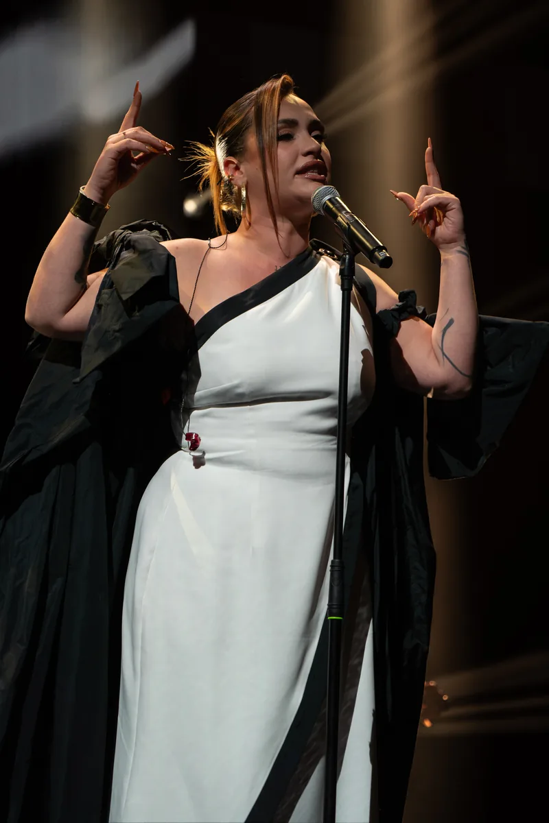 Lia Kali cantando ante el micrófono con los brazos levantados