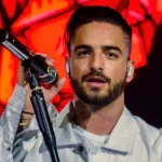 Maluma canta con el micrófono en la mano y chaqueta blanca