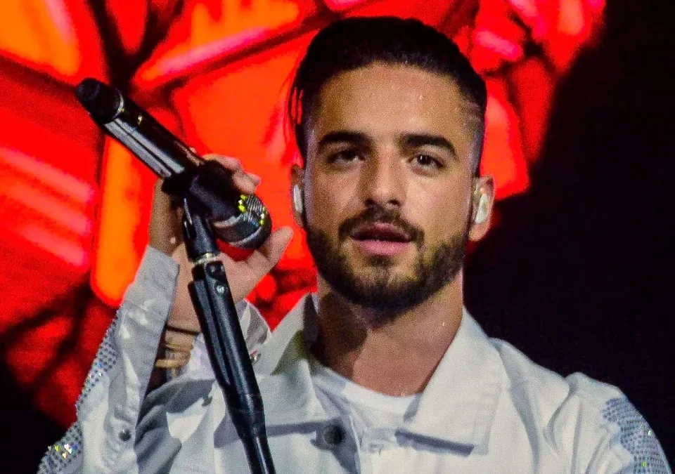Maluma canta con el micrófono en la mano y chaqueta blanca