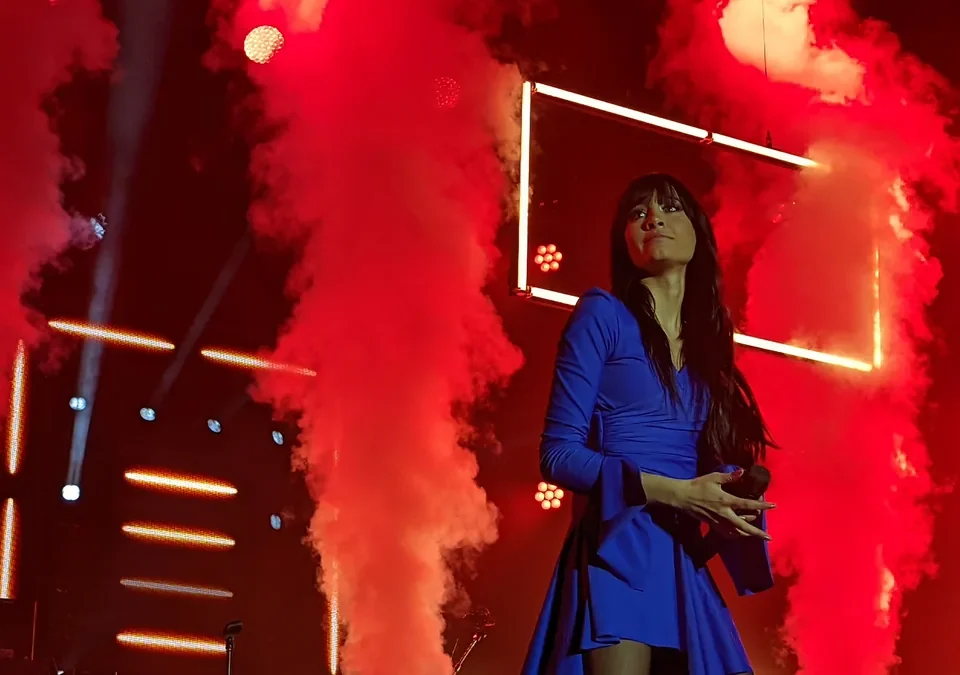 Aitana con vestido azul sobre el escenario, entre columnas de humo rojo
