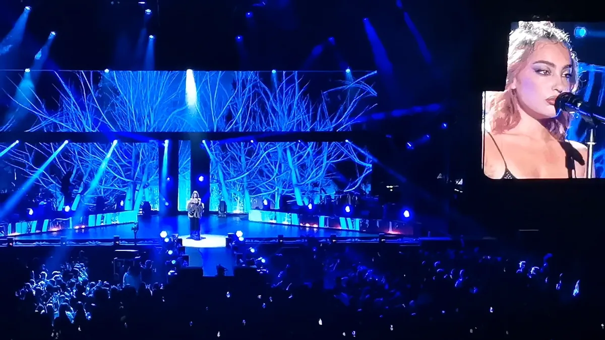 Violeta Hódar cantando en un escenario iluminado de azul, con su cara en la pantalla gigante