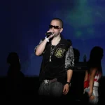 Yandel cantando sobre el escenario con un micrófono en la mano