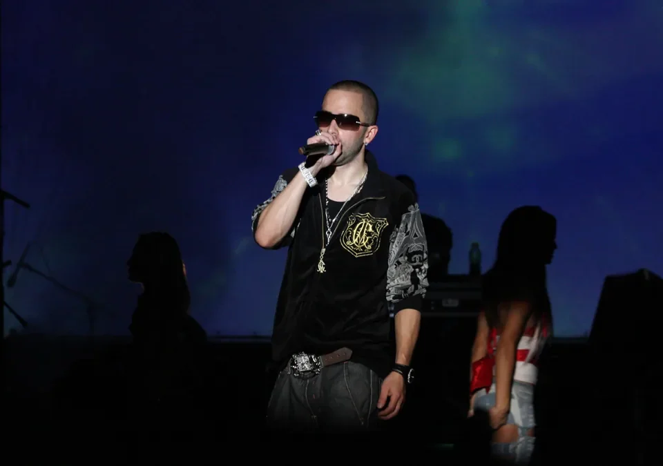 Yandel cantando sobre el escenario con un micrófono en la mano